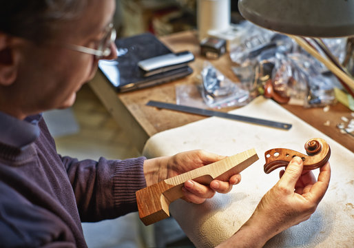 Violin maker in his workshop examining neck and scroll of an instrument