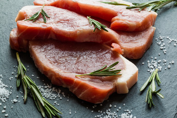 Raw pork steaks with rosemary on black stone background.