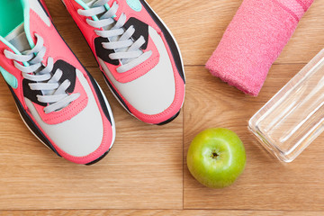 red and grey sneakers with grey shoelaces and red towel, green apple, bottle with water on wooden background indoors