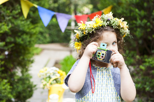 Little girl wearing flowers taking a picture with vintage camera