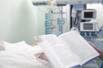 Doctor reading book at the patient bed