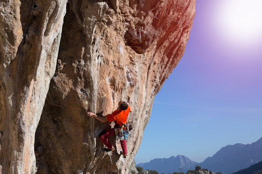 Athlete climbs on a rock against mountains.