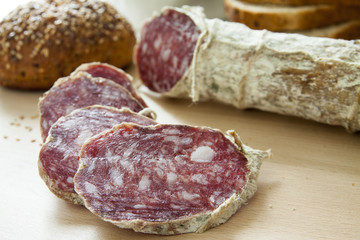 Salame casereccio a fette con pane integrale su tagliere di legno