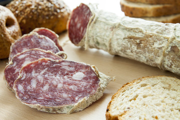Salame casereccio a fette con pane integrale su tagliere di legno