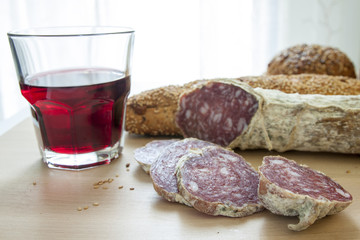 Salame casereccio a fette con pane integrale e bicchiere di vetro di vino rosso