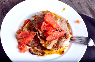 Beef with grapefruit sauce on wood background