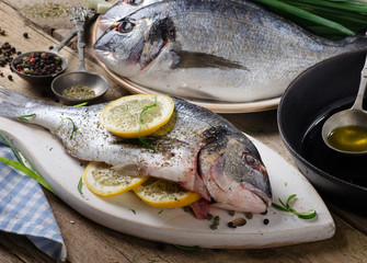 Fresh uncooked dorado with lemon, oil and spices on a wooden boa