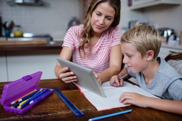 Mother using tablet while helping son with his homework