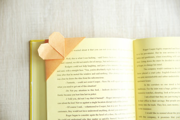 Book and heart shaped bookmark on a light wooden background