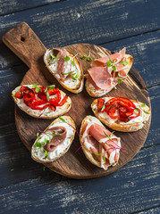 Sandwiches with goat cheese, anchovies, roasted peppers, ham on a wooden rustic board. Delicious snack or appetizer with wine