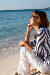 Fototapeta na wymiar femme assise à la plage au téléphone