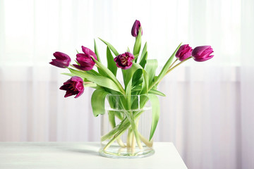 A bouquet of violet tulips in a vase on white table.