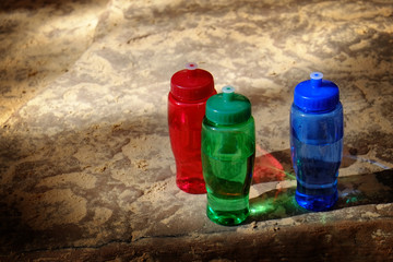 Red, Green, Blue Water Bottles on Rough Rocks