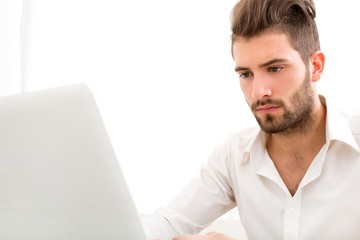 Attractive young man sitting at the table with a laptop computer..