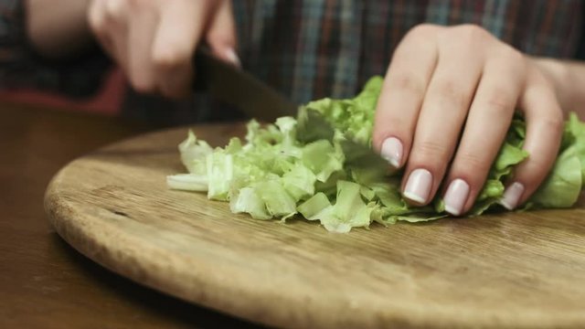 Woman shredding fresh green cabbage by big knift  on a cutting board in the kitchen.