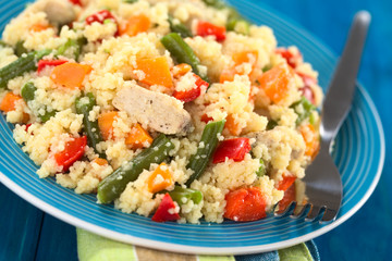 Couscous dish with chicken, green bean, carrot and red bell pepper served on plate with fork on the side (Selective Focus, Focus on the meat in the middle of the image)