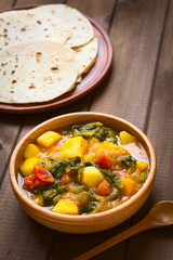 Pumpkin, mangold, potato and tomato curry dish with homemade chapati flatbread in the back photographed with natural light (Selective Focus, Focus in the middle of the curry dish)
