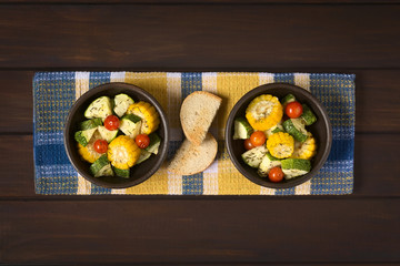 Baked vegetables of sweet corn, zucchini, cherry tomato with thyme, toasted bread slices in the middle, photographed on dark wood with natural light