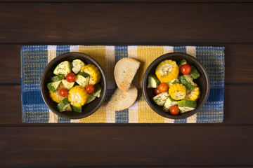 Baked vegetables of sweet corn, zucchini, cherry tomato with thyme, toasted bread slices in the middle, photographed on dark wood with natural light
