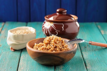 Wholegrain spelt porridge with butter in wooden bowl and raw spe