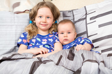 Two sisters. Older sister kid hugging his newborn little sister. Cute children girls on bed at home.