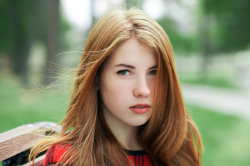 Closeup portrait of young adorable redhead woman in red plaid jacket with blurred park background