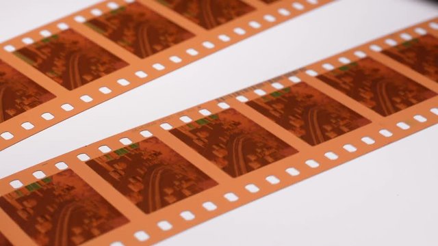 Using a magnifying glass to examine a 35mm movie filmstrip negative on a light table.