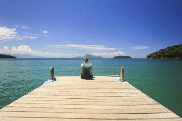 Fototapety  podróżnik siedzący na molo w oceanicznej plaży z zieloną wodą