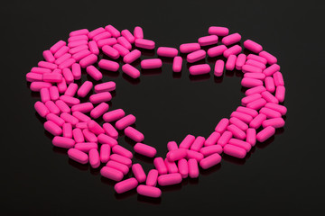 Pills, vitamins on black background in shape of the heart