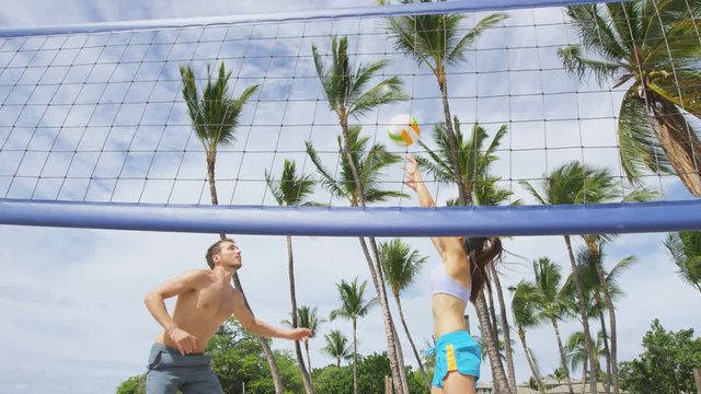 Friends playing beach volleyball sport in summer. Woman volley the ball to man jumping to smash. People having fun recreational volley ball game living healthy active sport lifestyle. RED EPIC. 