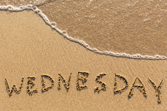 Week series - WEDNESDAY - written on a sandy beach with the soft wave at sunny day.