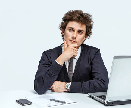 Take thought. Young Businessman at the workplace working with computer on gray background.