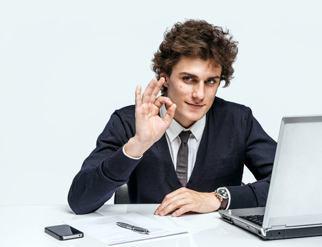 Cheerful young businessman showing Its Okay. Businessman at the workplace working with computer on gray background.