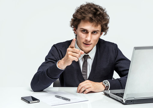 Purposeful Manager looking at camera with serious look indicates for you. Businessman at the workplace working with computer on gray background.