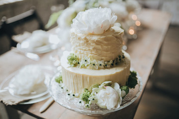 white cake decorated with flowers, berries and greens costs on a wooden table decorated loft with white brick walls and wooden floor