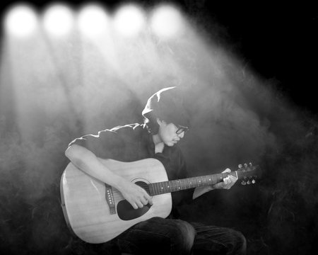 Man playing guitar with spotlight and smoke., Black and white photo.