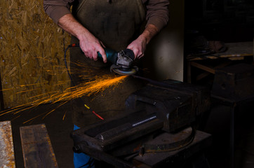 Man cutting steel by grinder in forge.