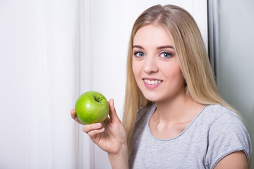 young woman holding green apple at home