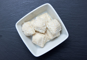 Cakes with coconut on a square bowl on slate top seen from above
