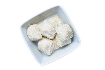 Cakes with coconut on a square bowl on a white background seen from above