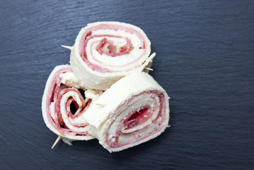 Rolls of flat bread with salami on slate top seen from above