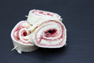 Rolls of flat bread with salami on top in slate
