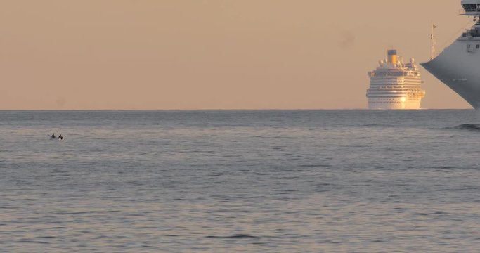 nave da crociera sfila molto vicino ad una piccola barca a remi e sullo sfondo un'altra nave da crociera