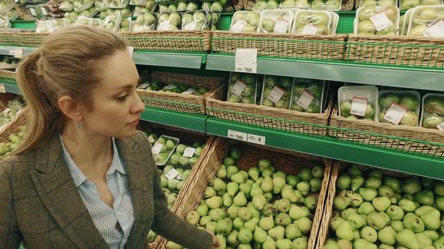 Young blond woman sniffs the pear in supermarket