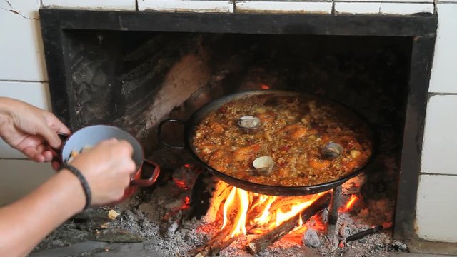 Cocinando una paella al fuego de le&ntilde;a
 -  Mujer Echando almejas a una paella de marisco cocinada al fuego de le&ntilde;a
