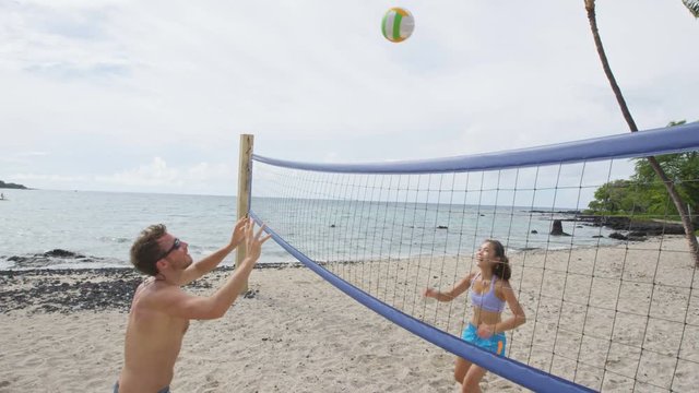 Couple playing beach volleyball having fun in sporty active lifestyle. Man hitting volley ball in game in summer. Woman and man fitness model living healthy lifestyle doing sport on beach.