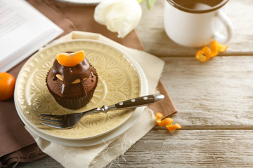 Tasty cupcake with slice of mandarin and chocolate on a plate over light wooden background