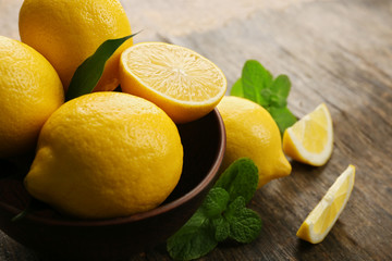 Fresh lemons with green leaves in bowl on wooden background