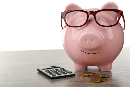 Pink piggy bank with coins, glasses and calculator on white background