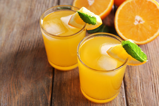 Two orange juices with ice and orange on, closeup